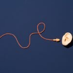 Orange Ear Plugs with Curved String Reach to Ear on Blue Background Directly above View. 4 tips for RevOps teams to filter out the noise and focus on the big picture