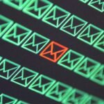 a pattern of green email envelopes on a black background, with a single red email envelope to signify a malicious email