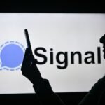 silhouette of person looking at phone in front of Signal logo