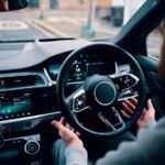 person's hands letting go of steering wheel of self-driving car