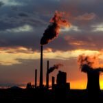 Coal power station with smoking chimneys at sunset against a cloudy sky.