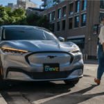 Woman walks up to silver Mustang Mach-E. License plate says "Ford Drive"
