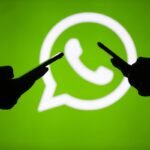 People hold mobile phones in front of the logo of WhatsApp application.