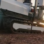 An autonomous, tracked robot sits on a dirt patch.