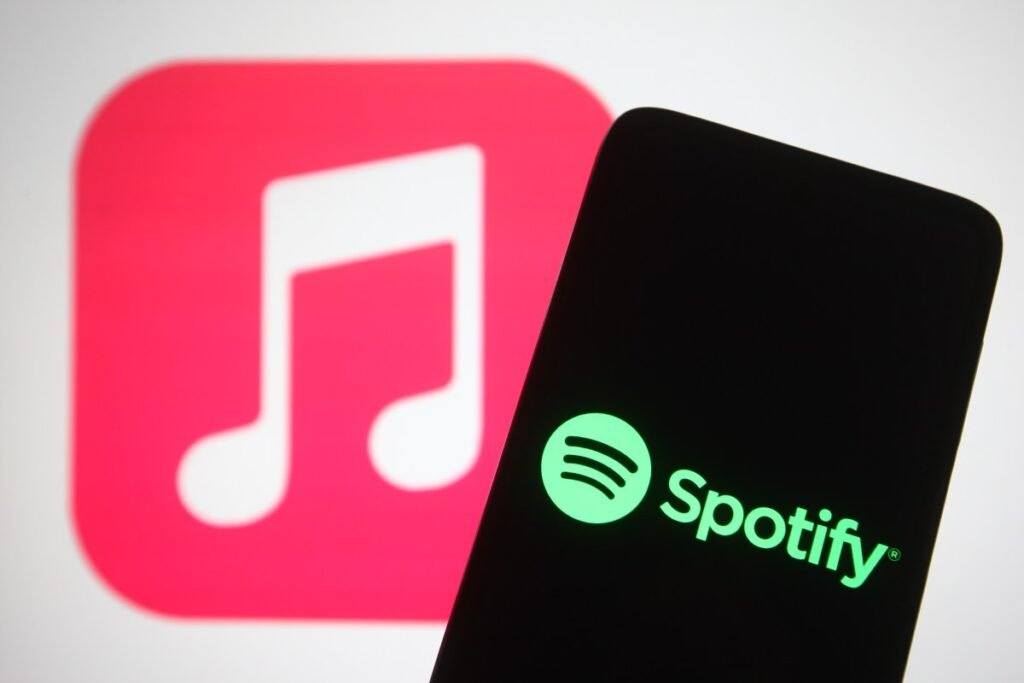 The Spotify logo seen displayed on a smartphone screen in front of Apple Music logo in the background.