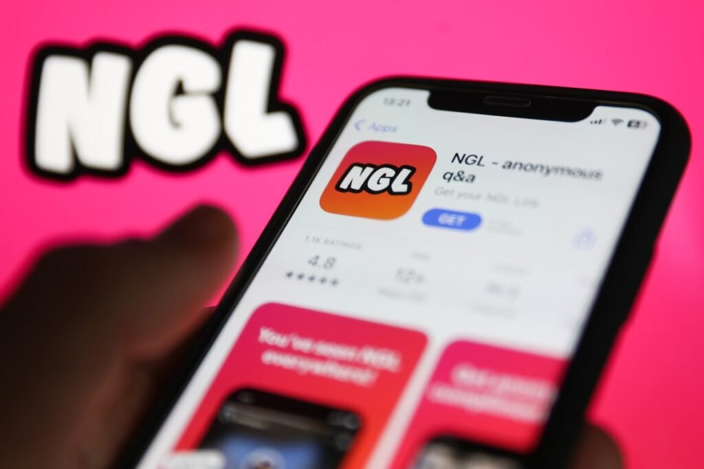 NGL on App Store displayed on a phone screen and NGL website displayed on a screen in the background are seen in this illustration photo