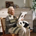 woman sits, reading, with a cuddly AI baby panda robot on her lap