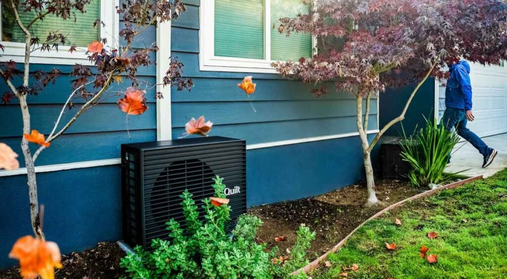 A dark grey heat pump sits outside a blue home.