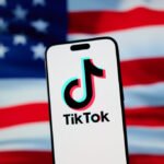 The TikTok app and logo are seen on a mobile device in front of a US flag