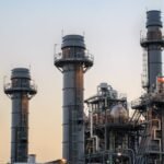 Natural gas power plant smoke stacks stand against a twilight sky.