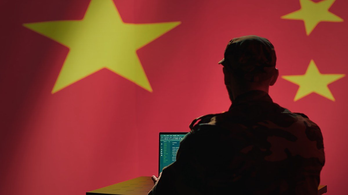 A man sits in front of a computer and the Chinese flag.
