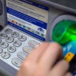 a close-up photo of a person punching in their PIN on an ATM in a wall.