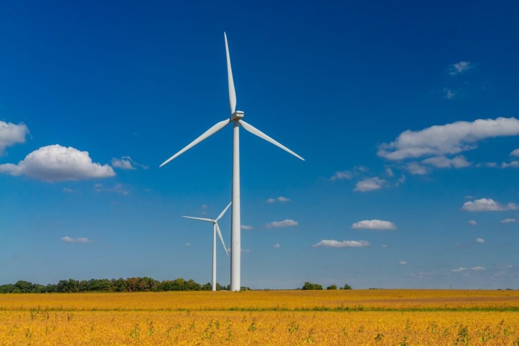 Two wind turbines stand against with a blue sky with cumulus clouds.