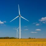Two wind turbines stand against with a blue sky with cumulus clouds.