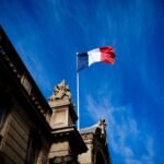 French tricolour flag (blue, white and red, symbol of the Republic of France) hanging from a flagpole above the entrance gate to the courtyard of the Elysee Palace, Exit from the Cabinet meeting at the Presidential Palace of the Elysee in Paris, France on August 27, 2025. The ministers get into their cars and leave the Elysee Palace. (Photo by Amaury Cornu / Hans Lucas via AFP)
