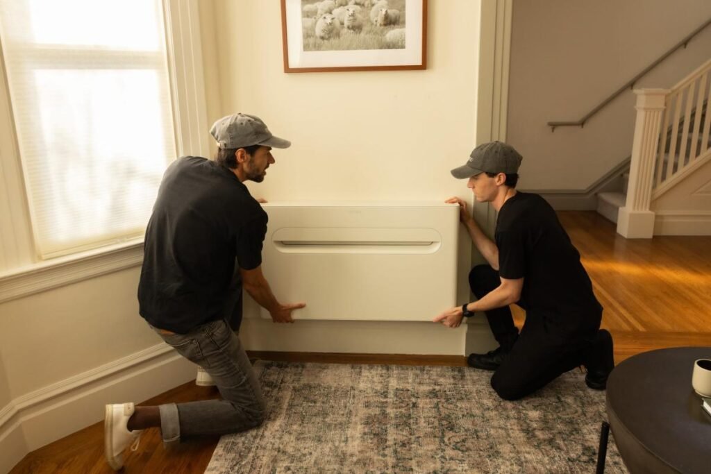 Two men install a heat pump on a wall.
