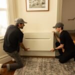 Two men install a heat pump on a wall.