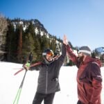 Two friends high-fiving while skiing.