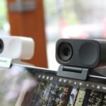 Duas pequenas webcams retangulares presas na parte superior da tela de um laptop, uma branca e outra preta