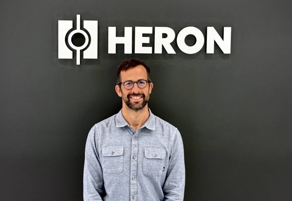 Drew Baglino standing in front of the Heron Power logo.