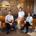Two men and a woman sit on leather chairs in a well appointed office space.