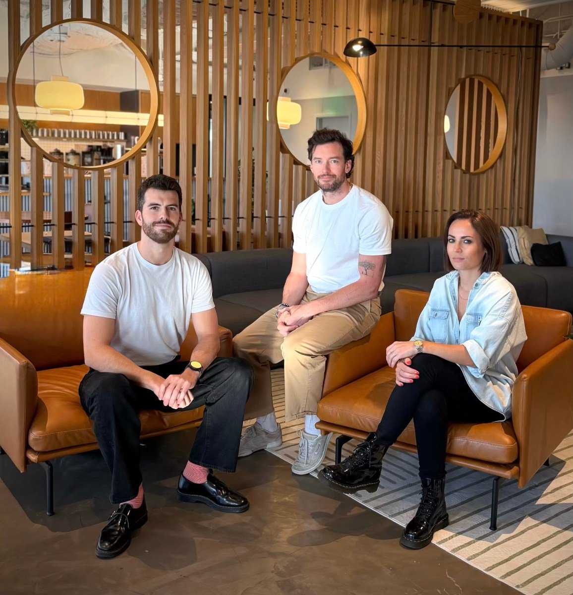 Two men and a woman sit on leather chairs in a well appointed office space.